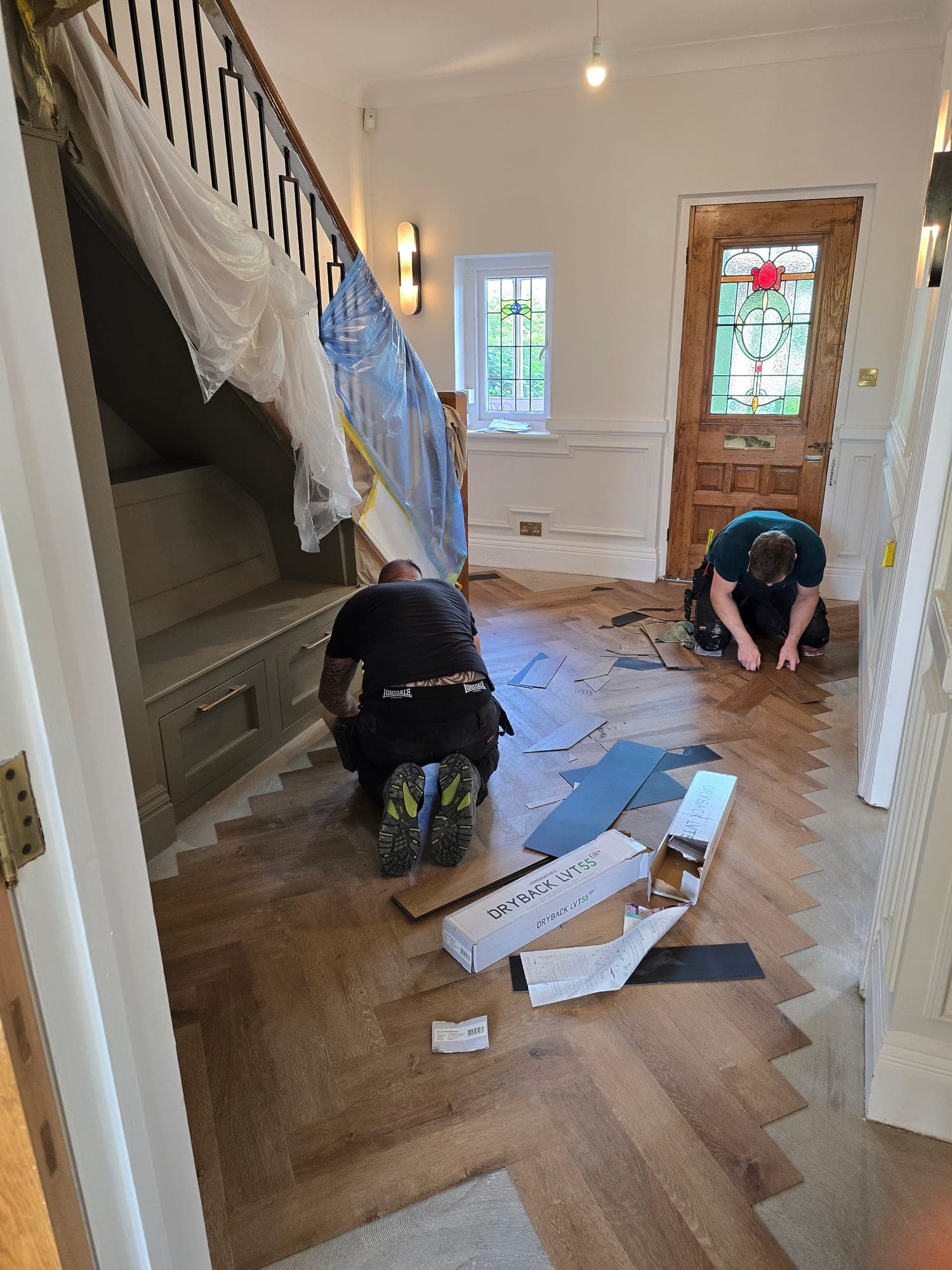 The herringbone floor being laid in the hallway, with the stained glass front door beyond