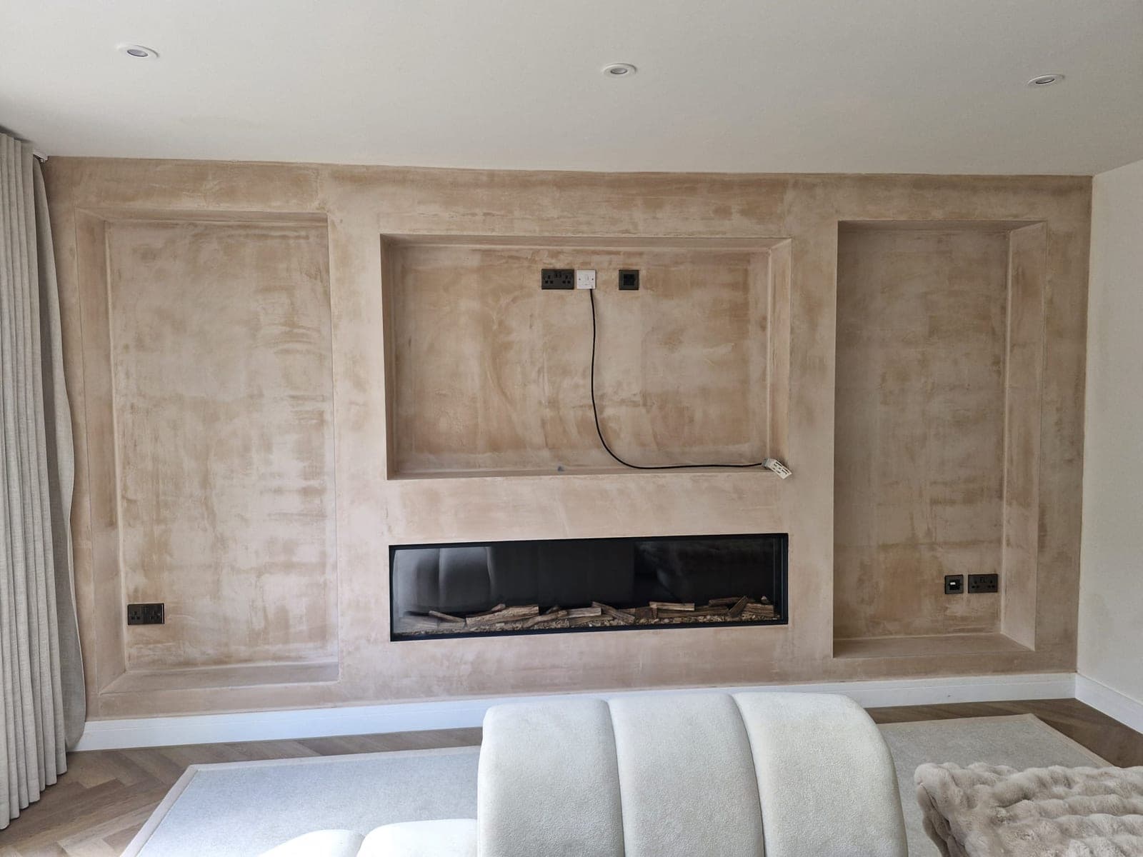 The rebuilt media wall in bare plaster, with the three openings formed and the linear fire fitted, before the joinery went in