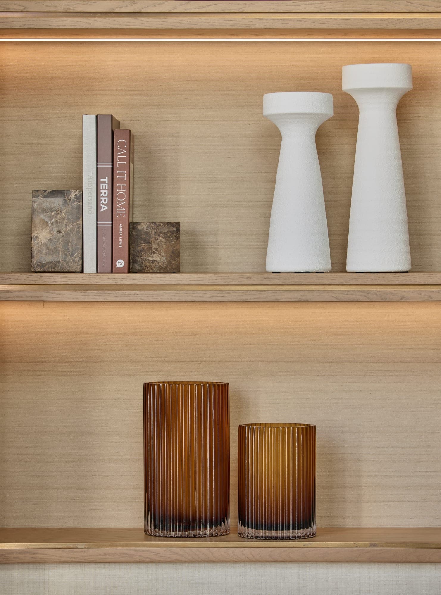 Lit oak shelves holding books with stone bookends, a pair of white vases and ribbed amber glass below