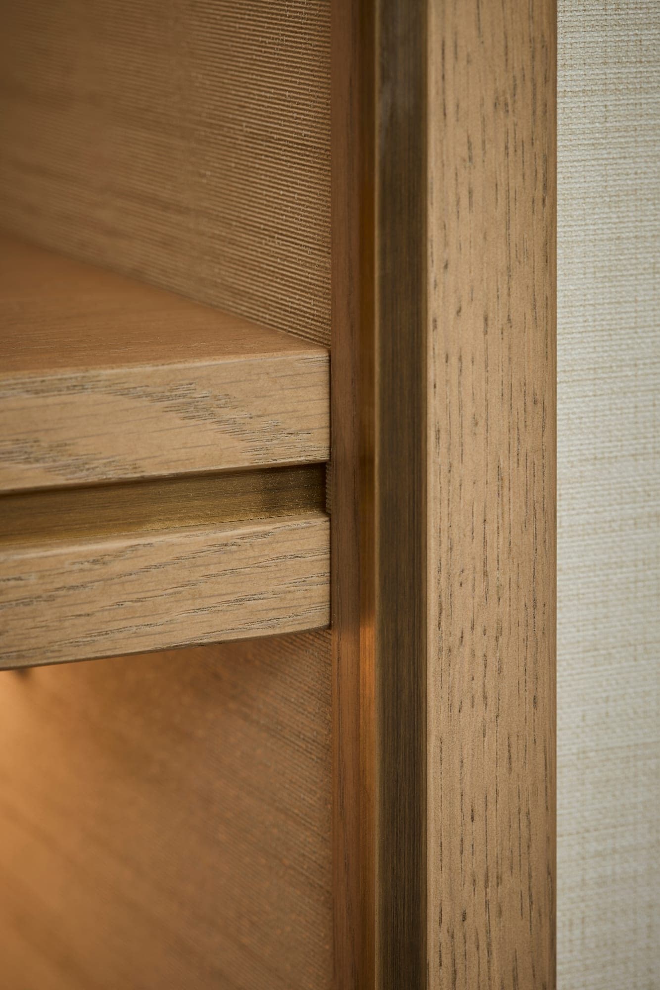 A close detail of the oak shelf edge, the bronze inlay along its front edge and the textured wallpaper behind