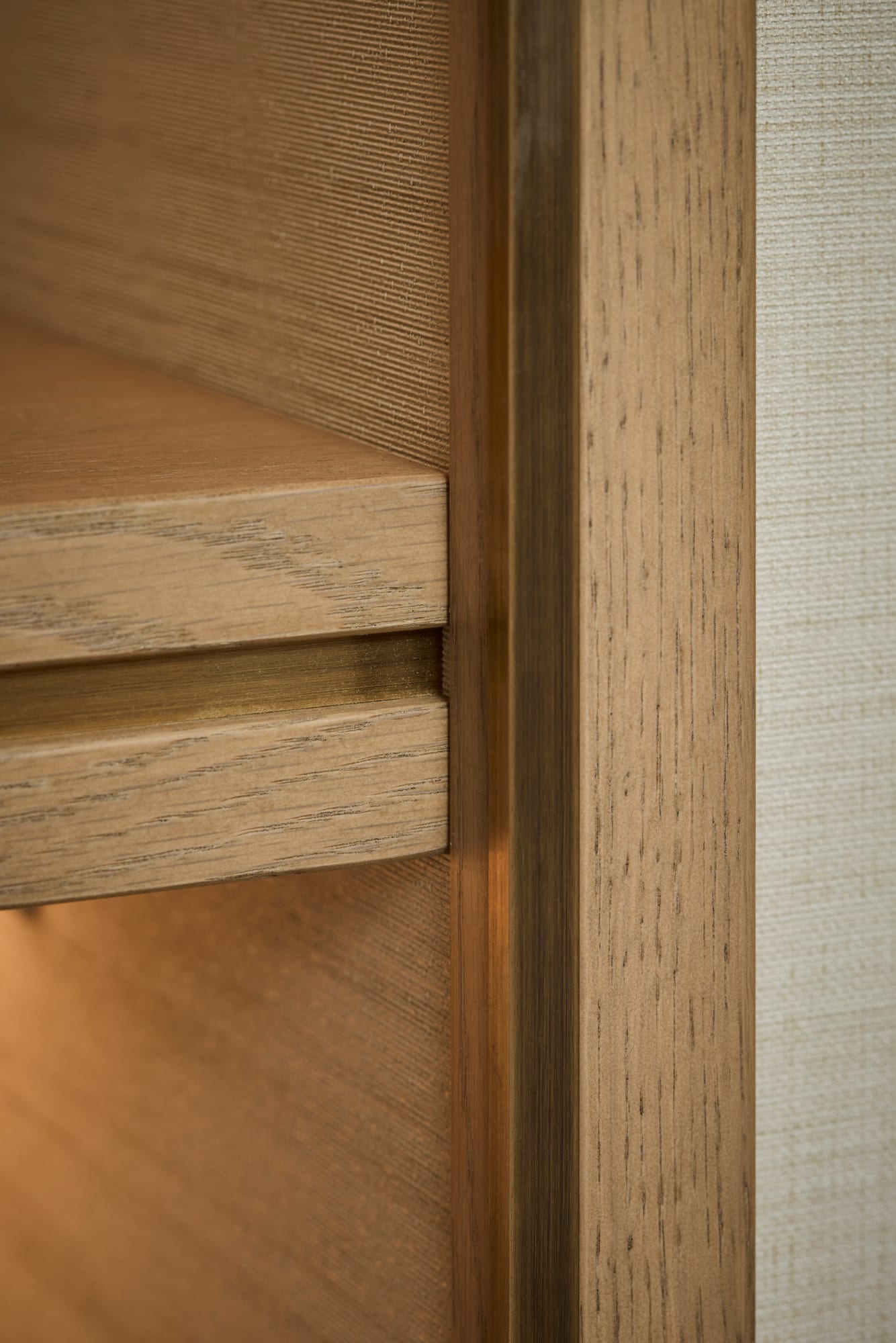 A close detail of the oak shelf edge, the bronze inlay and the textured wallpaper behind